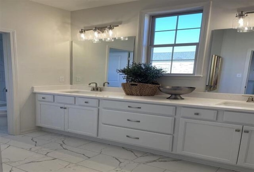 Dual vanity with white cabinetry and integrated sinks, quartz-finish countertop, brushed nickel hardware, and a window featuring grid-patterned muntins