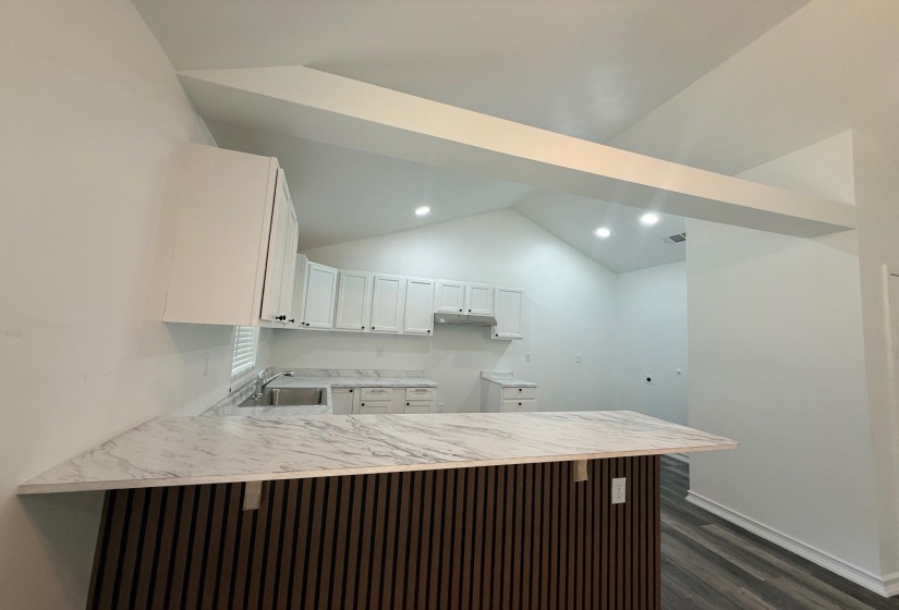 Kitchen featuring a custom breakfast bar with a wood-slat base and a marble-patterned countertop