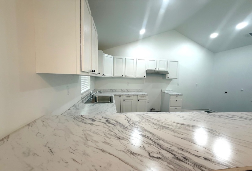 Kitchen featuring extensive white cabinetry, large undermount stainless steel sink, patterned countertops, and recessed lighting