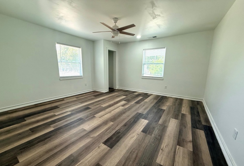 Spacious room with multi-toned wood-finish flooring, crisp white walls, and two large windows with blinds