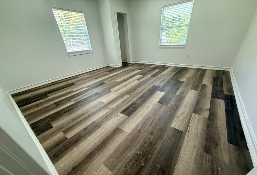 Spacious interior room featuring multi-toned wood-finish flooring, crisp white walls, and bright white trim