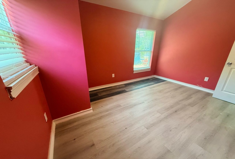 Spacious room featuring light wood-finish flooring, vibrant red walls, white baseboards, and a window with white blinds
