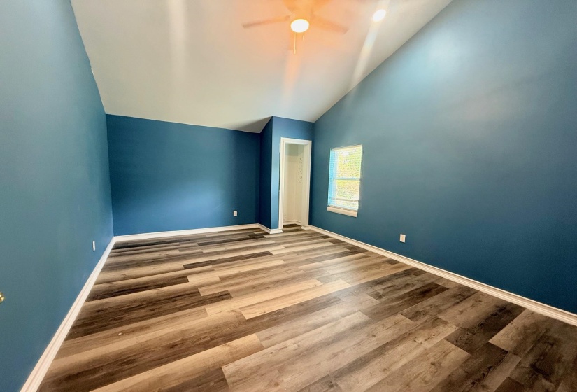 Spacious room featuring vaulted ceilings, a ceiling fan with integrated lighting, and a single window with blinds