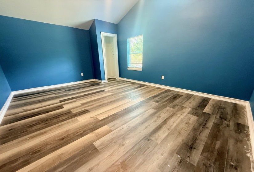 Spacious room featuring vaulted ceilings, wood-finish flooring, a window with blinds, and white trim