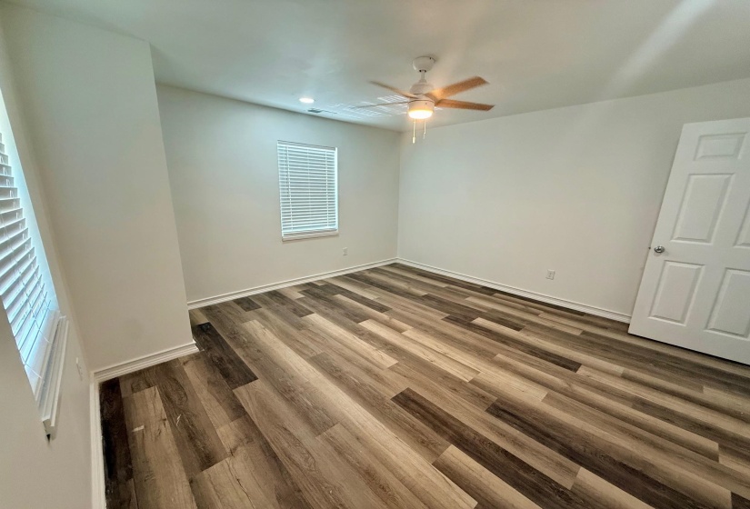 Spacious room featuring wood-finish flooring, white baseboards, and a ceiling fan with integrated lighting
