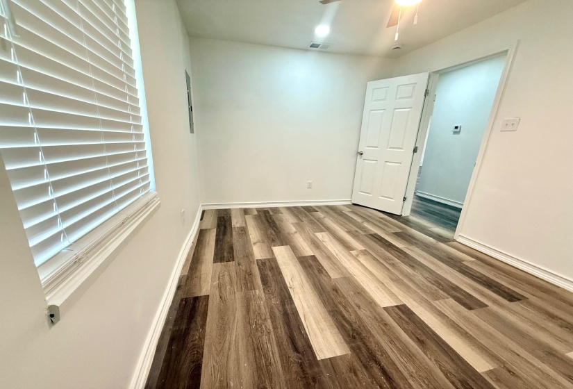 Spacious room featuring wood-finish flooring, white walls, and a ceiling fan with integrated lighting