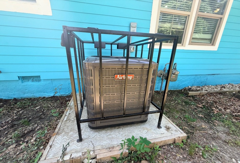 Exterior utility area featuring a central air conditioning unit on a concrete pad, enclosed by a metal security cage