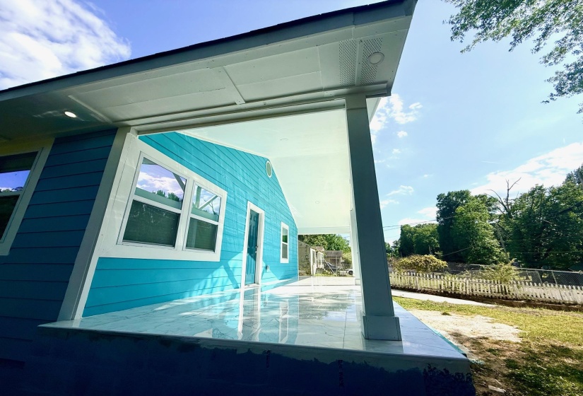 Expansive covered porch featuring a bright turquoise facade, white trim, recessed lighting, and a glossy tiled floor