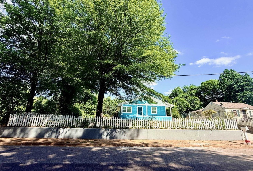 Blue exterior with white trim, featuring a white picket fence and mature trees