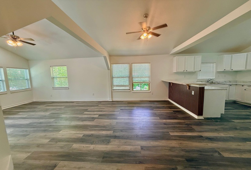 Vaulted ceilings with exposed beams and ceiling fans, wood-finish flooring, white kitchen cabinetry, and a peninsula with a breakfast bar