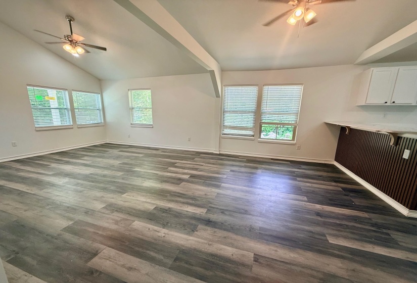 Spacious living area featuring wood-finish flooring, vaulted ceilings with exposed beams, and two ceiling fans
