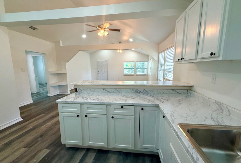 Kitchen featuring white cabinetry with dark hardware, a stainless steel sink, and light-toned countertops with a subtle marble-like pattern