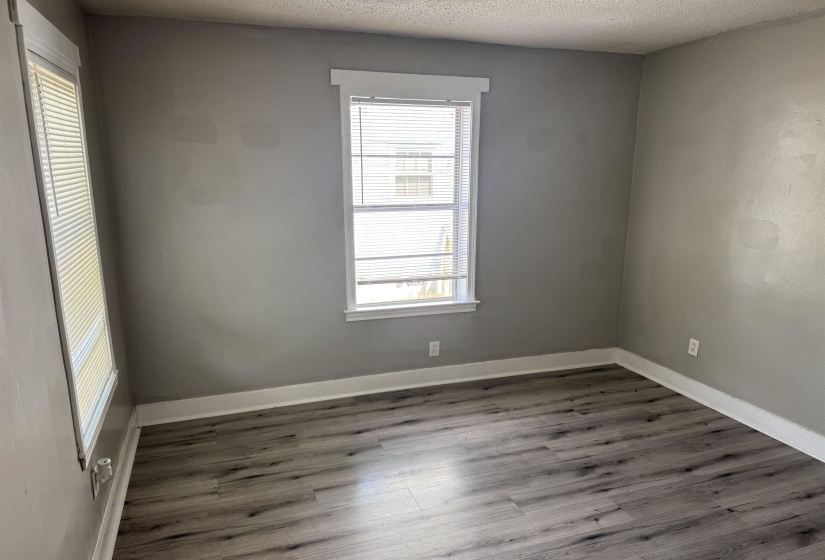 Room featuring two windows with horizontal blinds, wood-finish flooring, white baseboards, and neutral grey walls