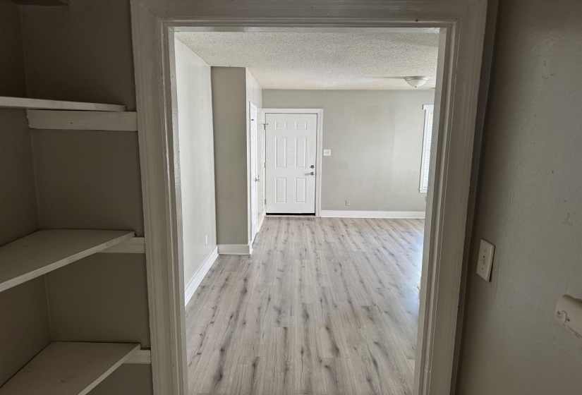 Interior space featuring light wood-finish flooring, neutral wall tones, white baseboards, a white paneled door, and built-in shelving