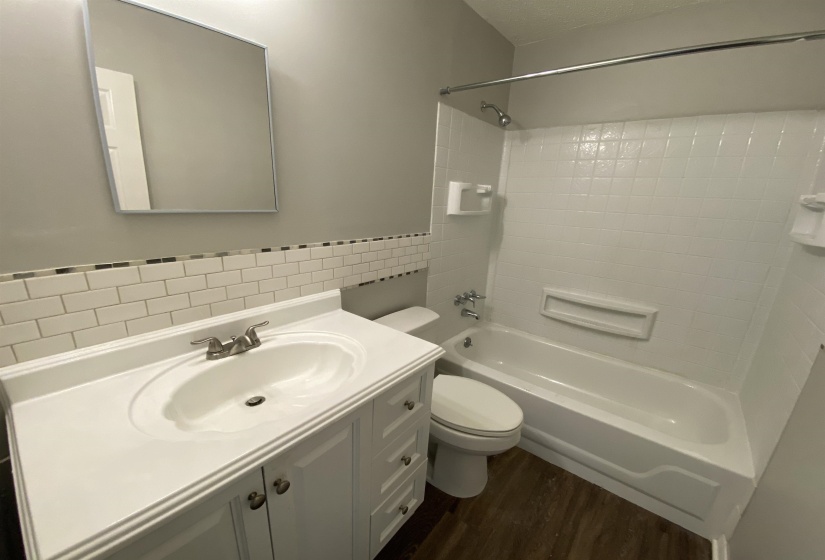 Bathroom featuring vanity, tub / shower combination, tile walls, dark wood-style floors, and wainscoting