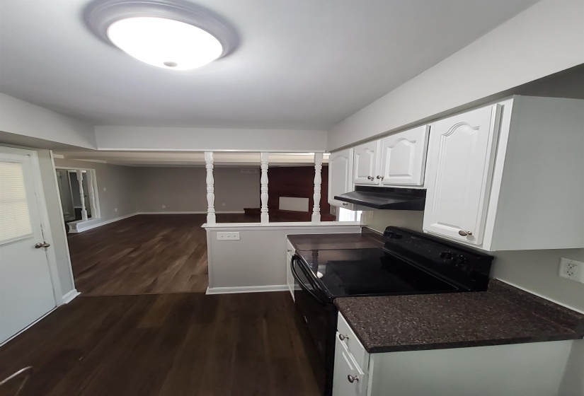 Kitchen featuring white cabinetry with decorative paneling, dark speckled countertops, and a black range with an overhead vent