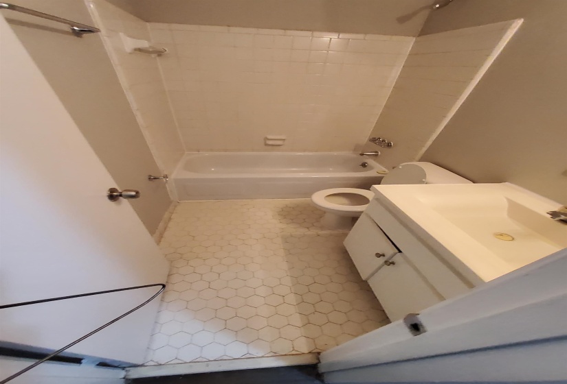 Bathroom featuring a white ceramic tile tub surround, white bathtub, hexagon floor tiles, white vanity with integrated sink, and chrome fixtures