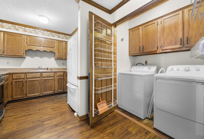 Kitchen and laundry area featuring wood-finish flooring, wood cabinetry, a built-in sink, and a refrigerator