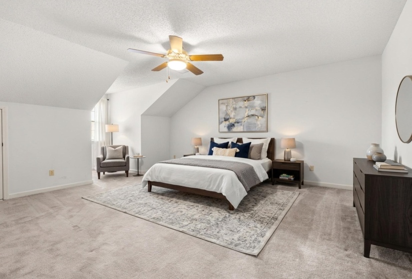 Spacious room featuring sloped ceilings, light-toned carpeting, a ceiling fan with integrated lighting, and a window with sheer curtains