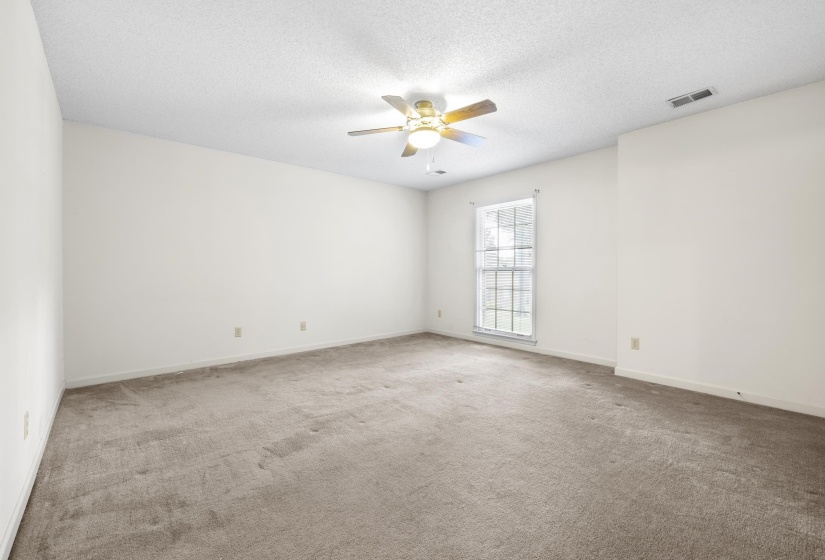 Spacious interior room featuring light-toned carpeting, white walls, and a textured white ceiling