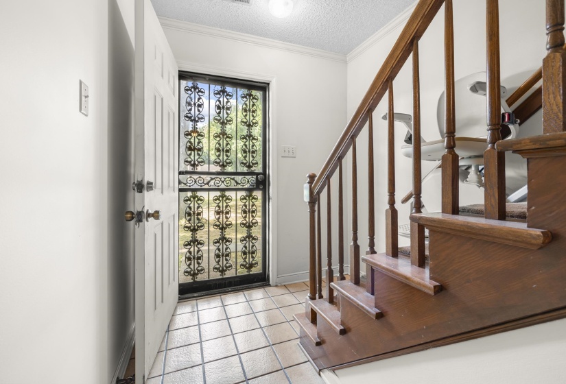 Entryway featuring tile flooring, a security screen door, and a hardwood staircase with a chair lift