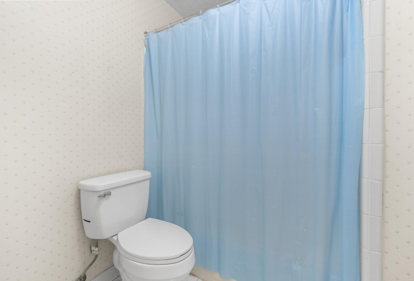 Bathroom featuring a standard toilet, white ceramic wall tiles, and patterned wallpaper