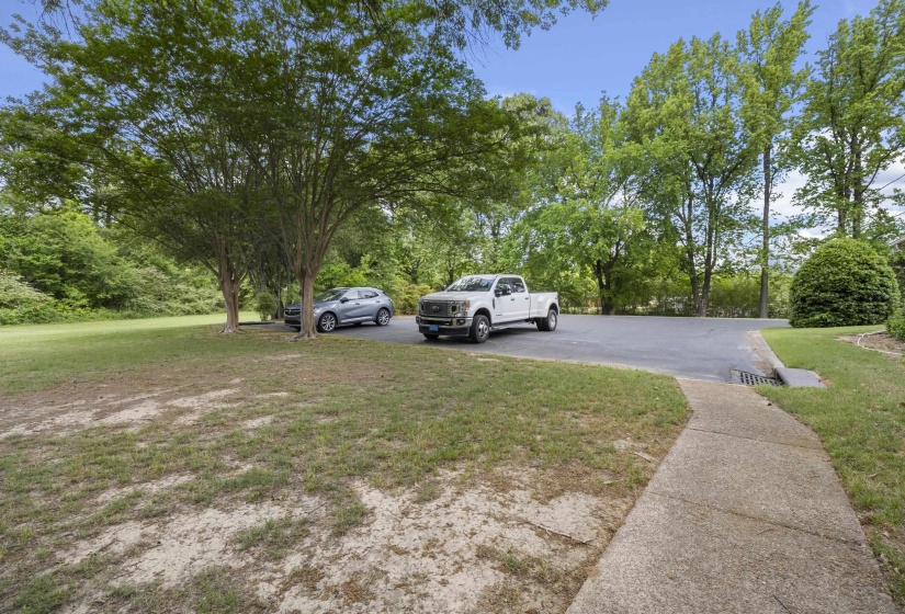 Paved driveway with ample parking space, bordered by a concrete walkway and mature trees