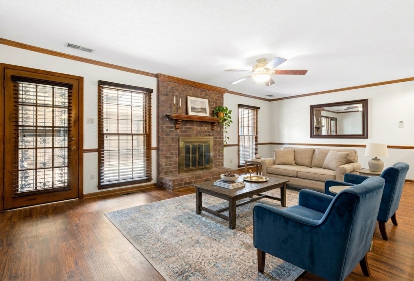 Expansive living area featuring a brick fireplace, wood-finish flooring, and crown molding