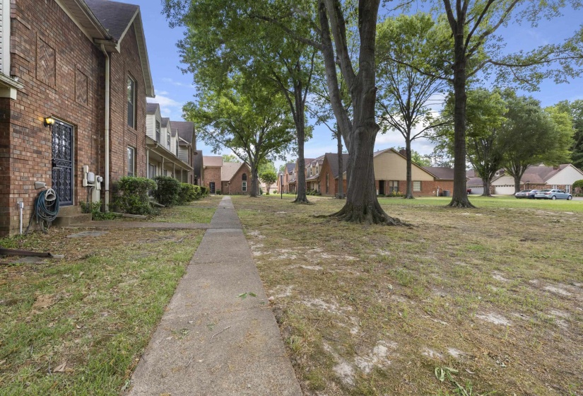 Brick exterior townhome with a concrete pathway and mature trees