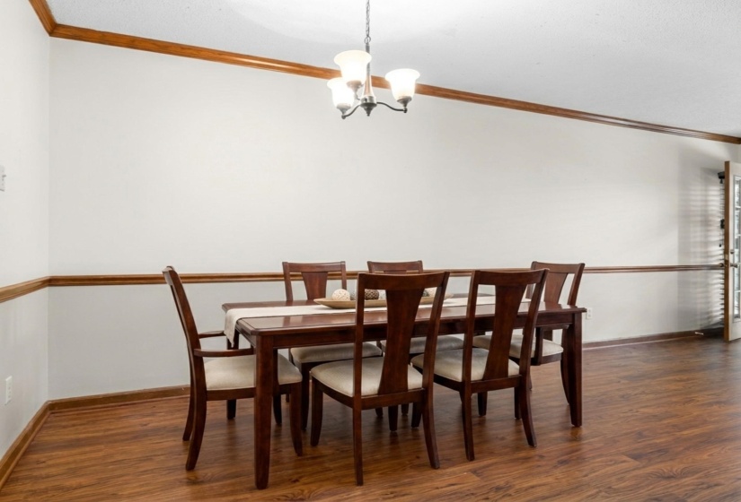 Dining space featuring wood-finish flooring, white walls with chair rail and crown molding, and a built-in chandelier