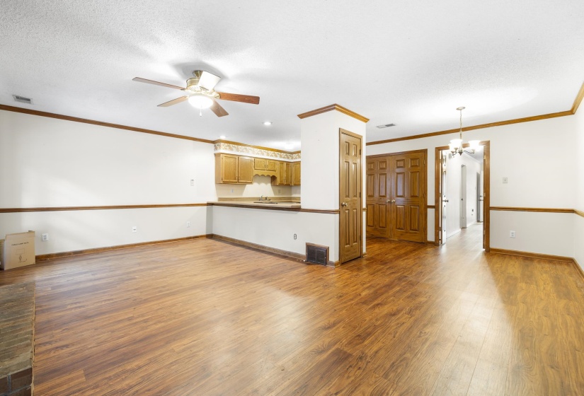 Open-concept living space featuring wood-finish flooring, a ceiling fan with integrated lighting, and a partial wall separating the kitchen area with wood cabinetry and countertop