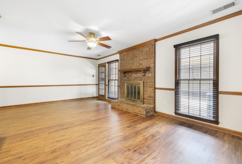 Spacious living area featuring wood-finish flooring, a brick fireplace with a wood mantle, and bright white walls with wood trim