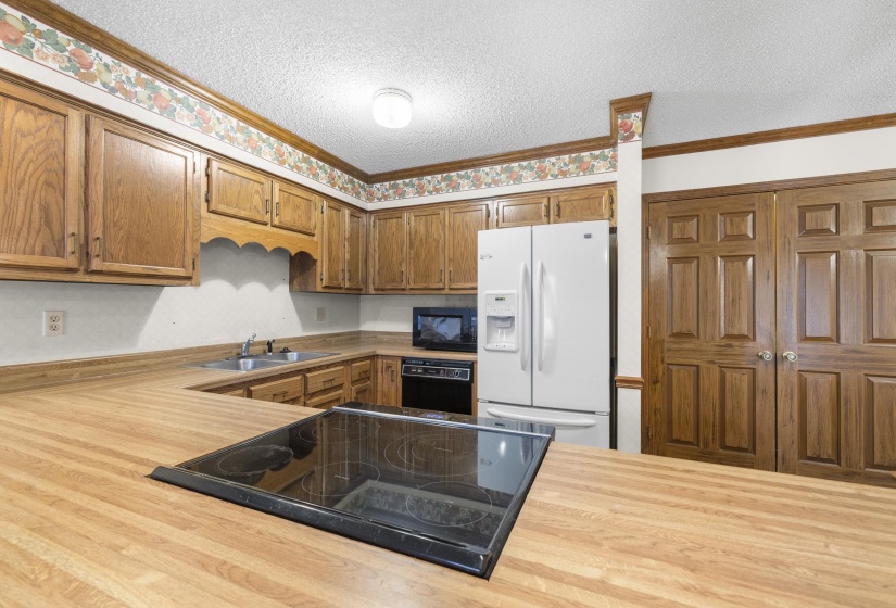 Kitchen featuring wood-finish countertops and cabinetry, a black electric cooktop, a double-basin stainless steel sink, and a white side-by-side refrigerator