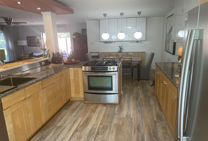 Kitchen with stainless steel appliances, light wood-type flooring, hanging light fixtures, dark stone countertops, and a ceiling fan