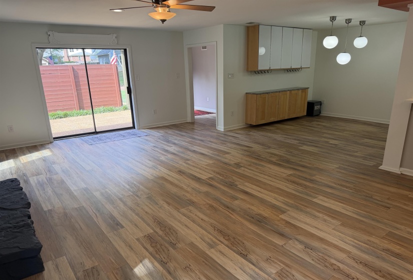Open-concept space featuring wood-finish flooring, a ceiling fan with integrated lighting, sliding glass door access to an outdoor area, and built-in cabinetry with a modern multi-light pendant fixture