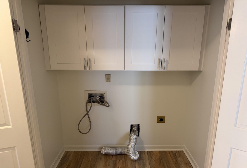 Dedicated laundry area featuring wood-finish flooring, crisp white walls, and built-in upper cabinetry with polished hardware