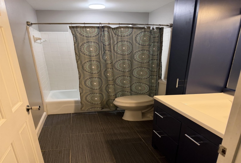 Bathroom featuring dark wood-finish tile flooring, a white porcelain tub with white subway tile surround, and a dark blue vanity with a white countertop and integrated sink