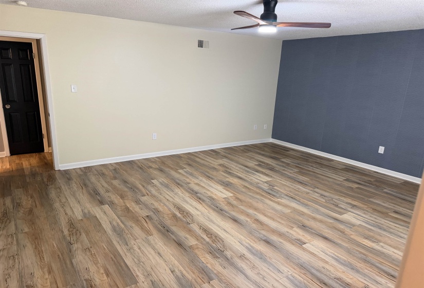 Spacious room featuring wood-finish flooring, a contemporary ceiling fan, a contrasting accent wall, and bright white baseboards