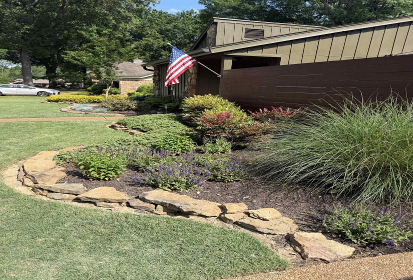 Curved natural stone landscaping elements complement the planted garden bed featuring various shrubs and flowering plants