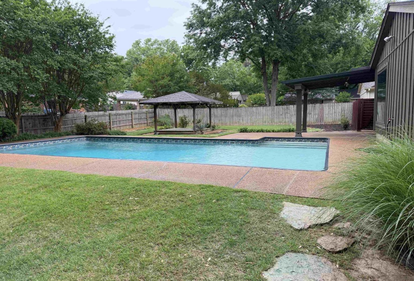 In-ground swimming pool featuring a textured concrete surround, adjacent to a covered patio