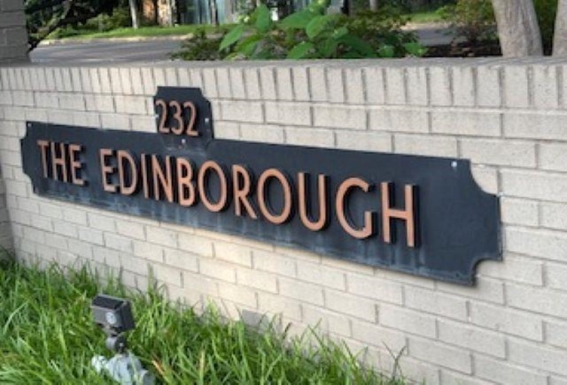 Property identification sign featuring a black base with raised copper-toned lettering, mounted on a light-colored brick wall