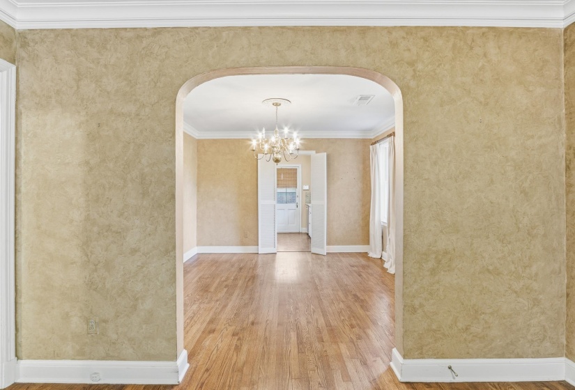 Arched entryway revealing wood-finish flooring, crown molding, and a chandelier