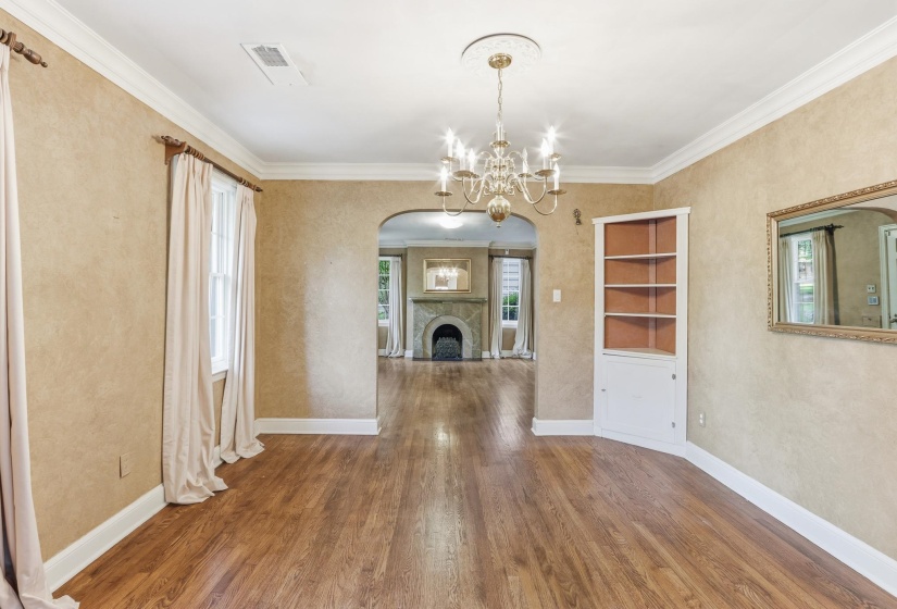 Spacious room featuring wood-finish flooring, a built-in corner cabinet with shelving, and an ornate chandelier