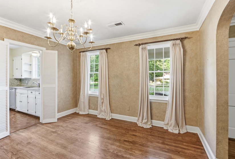 Room featuring wood-finish flooring, a brass chandelier, and two large windows with curtain rods