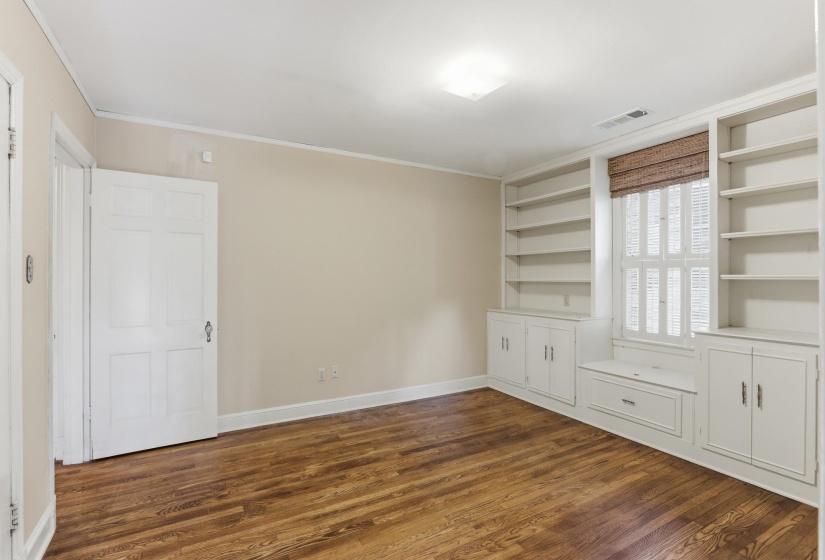 Room featuring hardwood flooring, extensive built-in shelving, integrated window seat with storage, white shutters, and a woven window treatment