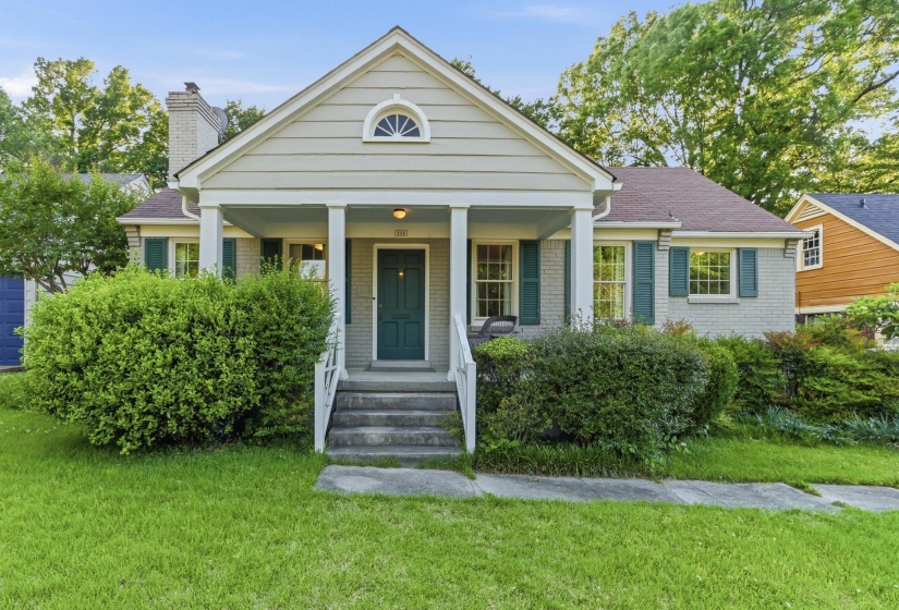 Traditional-style home featuring a covered front porch with white columns, a deep green entry door, and grey brick exterior with green shutters