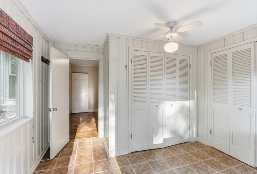 Room featuring light-colored tile flooring, white vertical wall paneling, and a white ceiling fan with integrated lighting