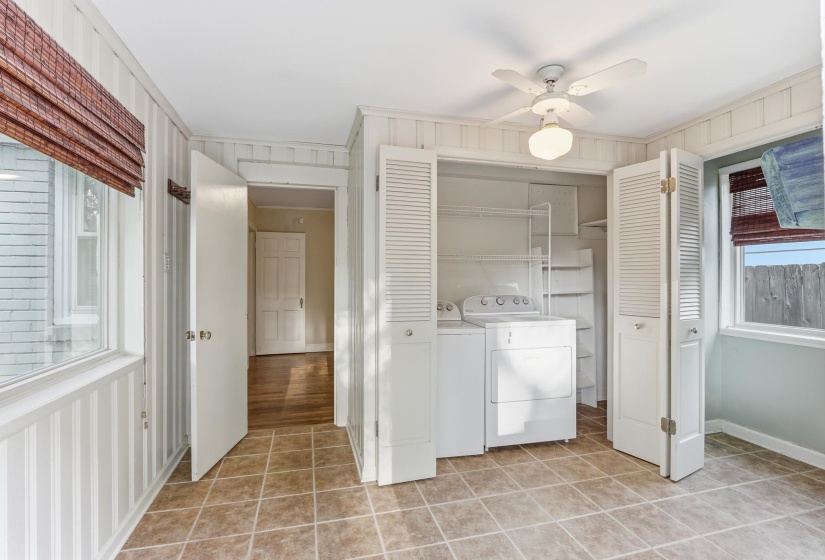 Laundry area featuring tile flooring, white vertical paneled walls, a ceiling fan with integrated lighting, and a utility closet with bifold louvered doors