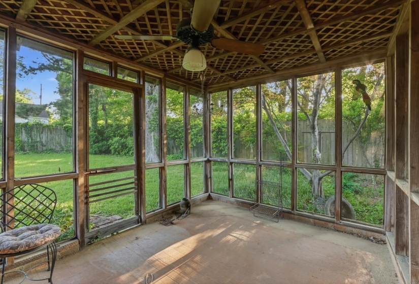 Screened-in porch featuring a lattice wood ceiling, large windows, wood-framed door, a ceiling fan with light fixture, and a concrete floor