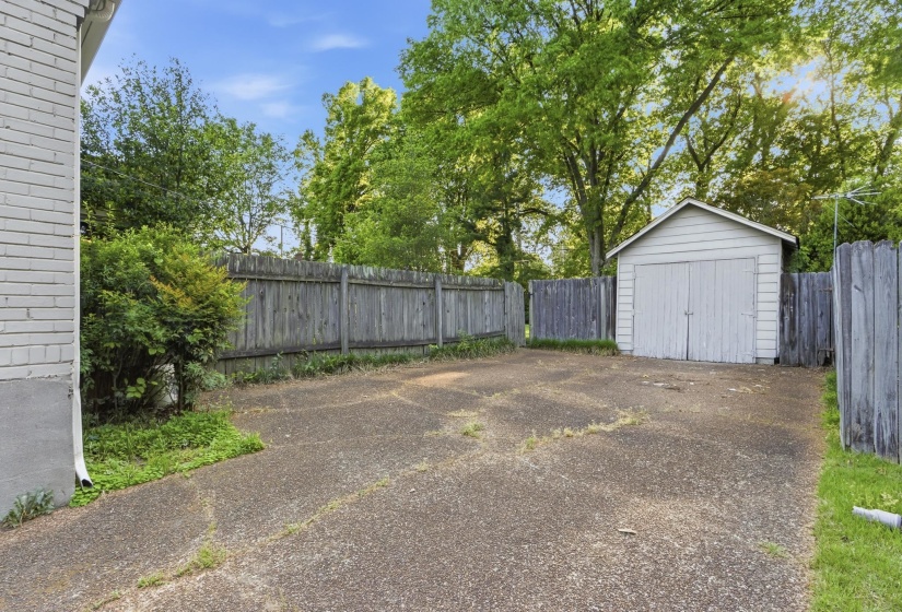 Detached storage shed with double doors, wood fencing, concrete driveway, and mature landscaping